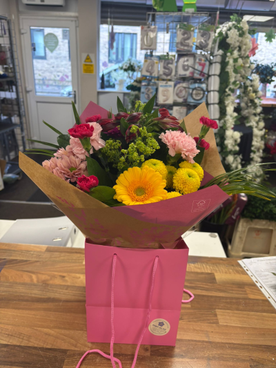 Raspberry Meadow Floral Bag - Colourful floral gift bag with vibrant seasonal blooms and cheerful tones in stylish pink packaging.